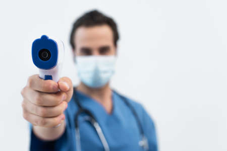 blurred doctor in medical mask holding pyrometer isolated on grayの写真素材
