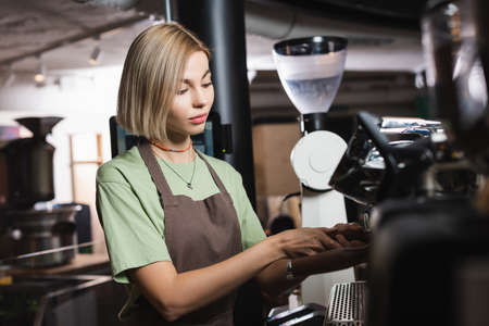 Blonde barista in apron working with coffee machine in cafeの写真素材