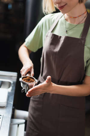 Cropped view of smiling barista holding portafilter with coffee in cafeの写真素材