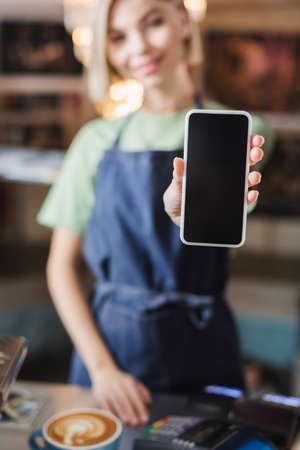 Smartphone with blank screen in hand of blurred barista in cafe
