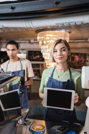 Barista holding digital tablet with blank screen near coffee and coffee machine in cafeの写真素材