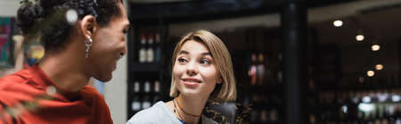 Smiling woman looking at african american boyfriend in cafe, banner