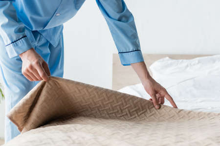 cropped view of man in blue pajamas covering bed with bedspread