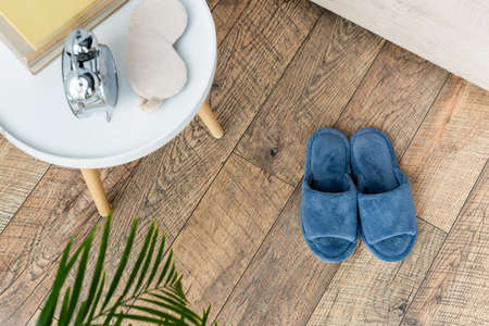 top view of soft slippers near bedside table with vintage alarm clock, sleep mask and books