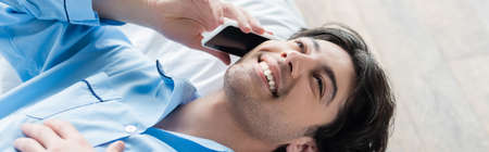 overhead view of young and happy man talking on smartphone on bed, banner