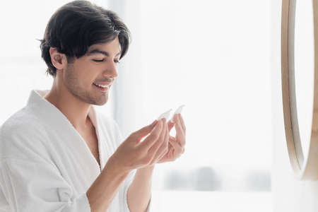 young brunette man smiling while holding cotton pads in bathroomの写真素材