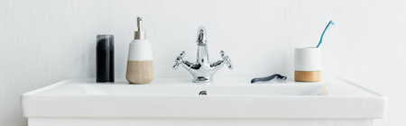 toothbrush, safety razor, liquid soap and shaving foam on white sink with faucet, banner