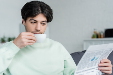 young brunette man drinking coffee and reading newspaper in the morning