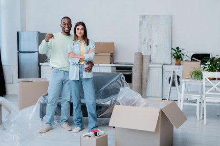 happy african american man holding key while hugging smiling girlfriend in new apartment