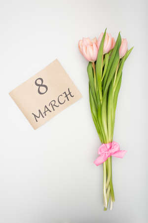 top view of pink tulips with ribbon near craft paper with 8 march lettering isolated on white