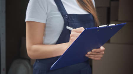 Cropped view of delivery woman writing on clipboard outdoors