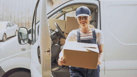 Smiling delivery woman holding cardboard box near car outdoorsの写真素材