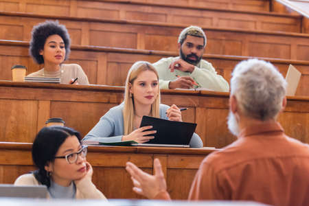Multicultural students looking at blurred teacher in university auditoriumの写真素材