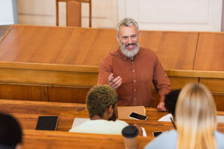 Smiling teacher talking near interracial students with notebooks in university