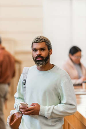 Young african american student with backpack and cellphone looking at camera in university
