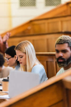 Young student sitting near coffee and interracial friends at universityの写真素材