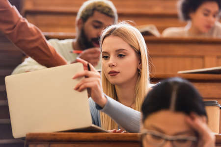 Young student using laptop near multiethnic friends at universityの写真素材