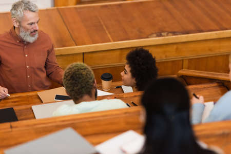 Smiling teacher holding chalk near african american students in university