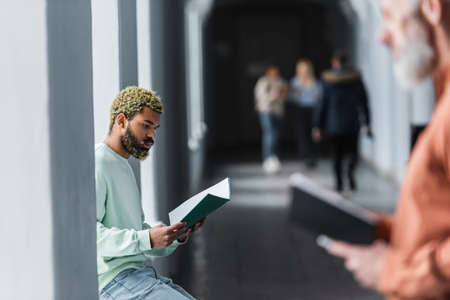 Young african american student looking at notebook near blurred teacher at universityの写真素材