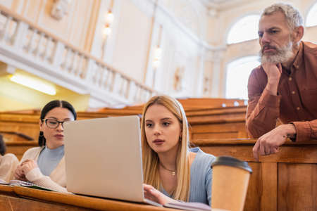 Teacher looking at laptop near interracial students in university