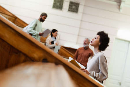 African american student holding notebook near blurred teacher and friends at university