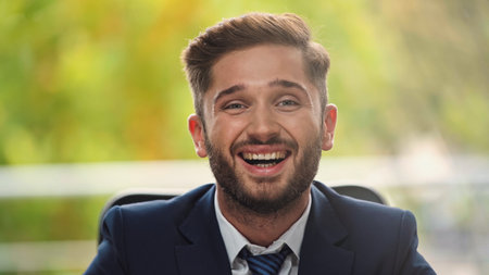 young and cheerful businessman laughing at camera in officeの写真素材