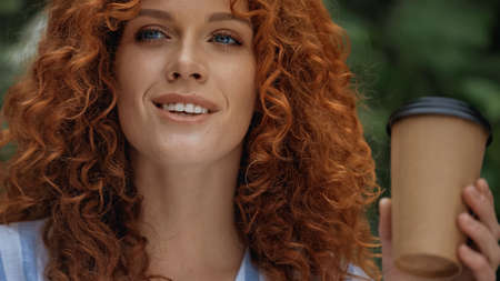 cheerful redhead woman with blue eyes holding paper cup outside