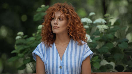 young redhead woman in striped dress waiting in park