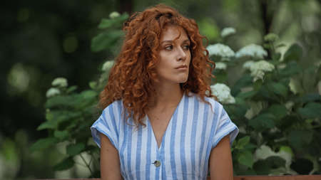 upset redhead woman in striped dress waiting in park