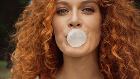 close up view of curly woman blowing bubble gumの写真素材