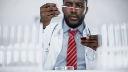blurred african american scientist looking at pipette with red liquid in labの写真素材