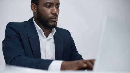 african american businessman using blurred laptop isolated on grayの写真素材