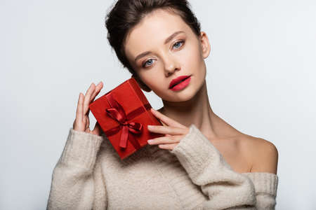 Brunette model in sweater posing with red gift isolated on whiteの写真素材