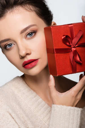 Stylish woman in sweater holding red gift box isolated on whiteの写真素材