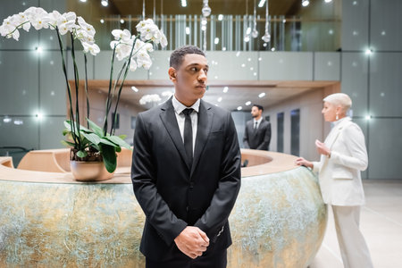african american security man looking away near blurred businesswoman at hotel reception