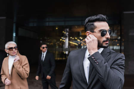 mixed race security man adjusting earpiece near senior businesswoman and african american guardの写真素材