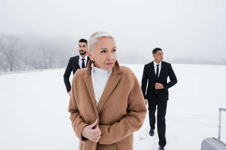 mature businesswoman looking away near multiethnic security men on snowy fieldの写真素材