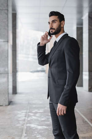 bi-racial security man in suit talking on mobile phone outdoorsの写真素材
