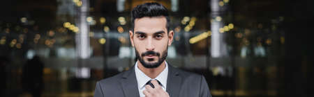 bearded mixed race guard adjusting tie and looking at camera outdoors, bannerの写真素材