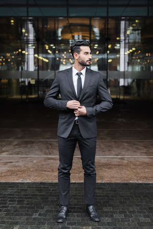 full length view of mixed race guard buttoning blazer and looking away near blurred hotel entranceの写真素材