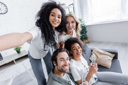 happy african american woman looking at camera with cheerful friends in living room
