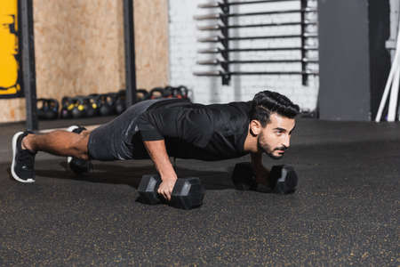 Arabian sportsman doing press ups with dumbbells in gym