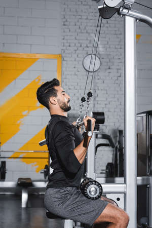 Side view of muslim sportsman training with lat pulldown machine in sports center