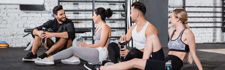 Positive multiethnic friends holding sports bottles in gym, banner