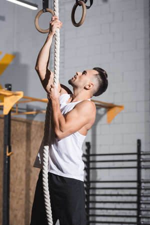 Side view of athletic sportsman climbing on rope in gym