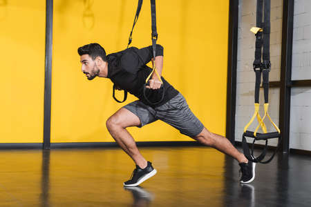 Side view of muslim sportsman working out with suspension straps in gymの写真素材
