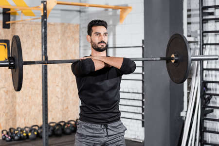 Arabian sportsman working out with barbell in blurred gym