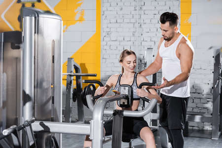 Trainer helping blonde sportswoman training on ab crunch machine in gym