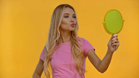 Blonde woman pouting lips while holding mirror isolated on yellowの写真素材