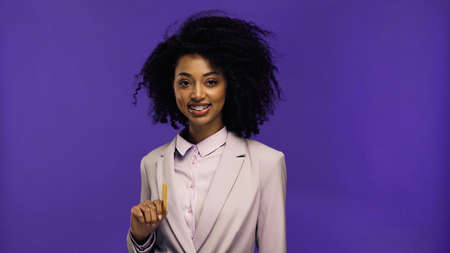 cheerful african american businesswoman with braces holding credit card isolated on purple